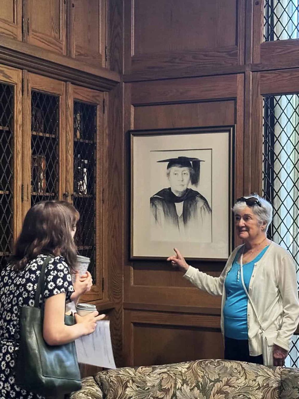 Old academic black-and-white portrait in wood-paneled room with two women discussing.