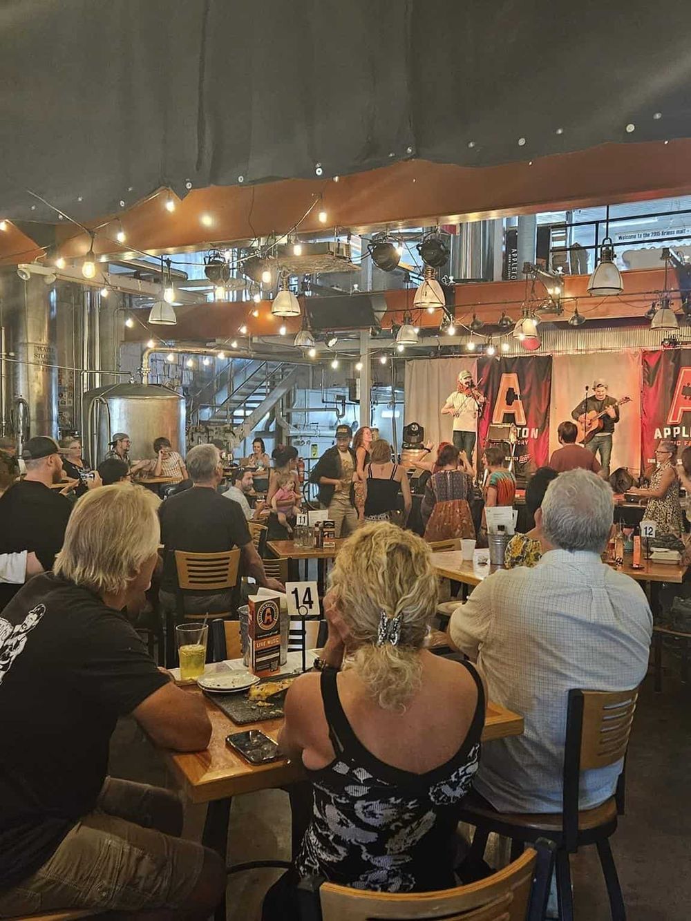 Live music at a brewery with a crowd enjoying a concert and drinks, vibrant atmosphere, and industrial decor.