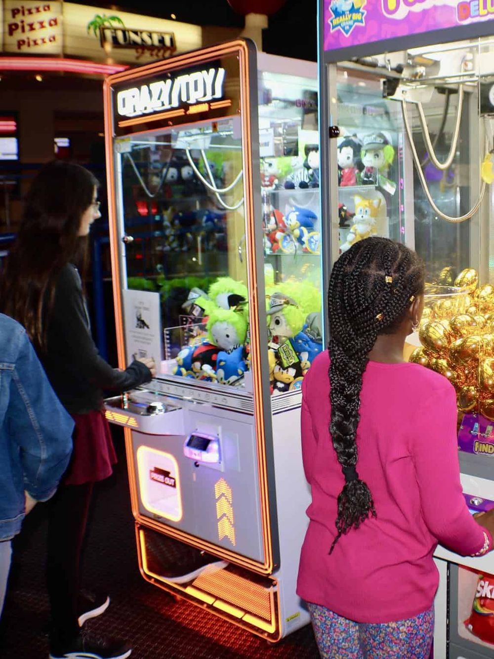 Colorful arcade claw machine with plush toys in a family entertainment center, kids playing and enjoying arcade games.