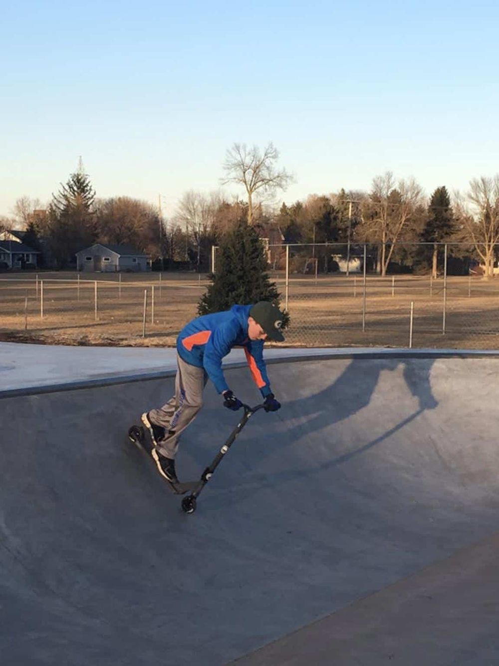 Youth riding scooter at skatepark during daytime.