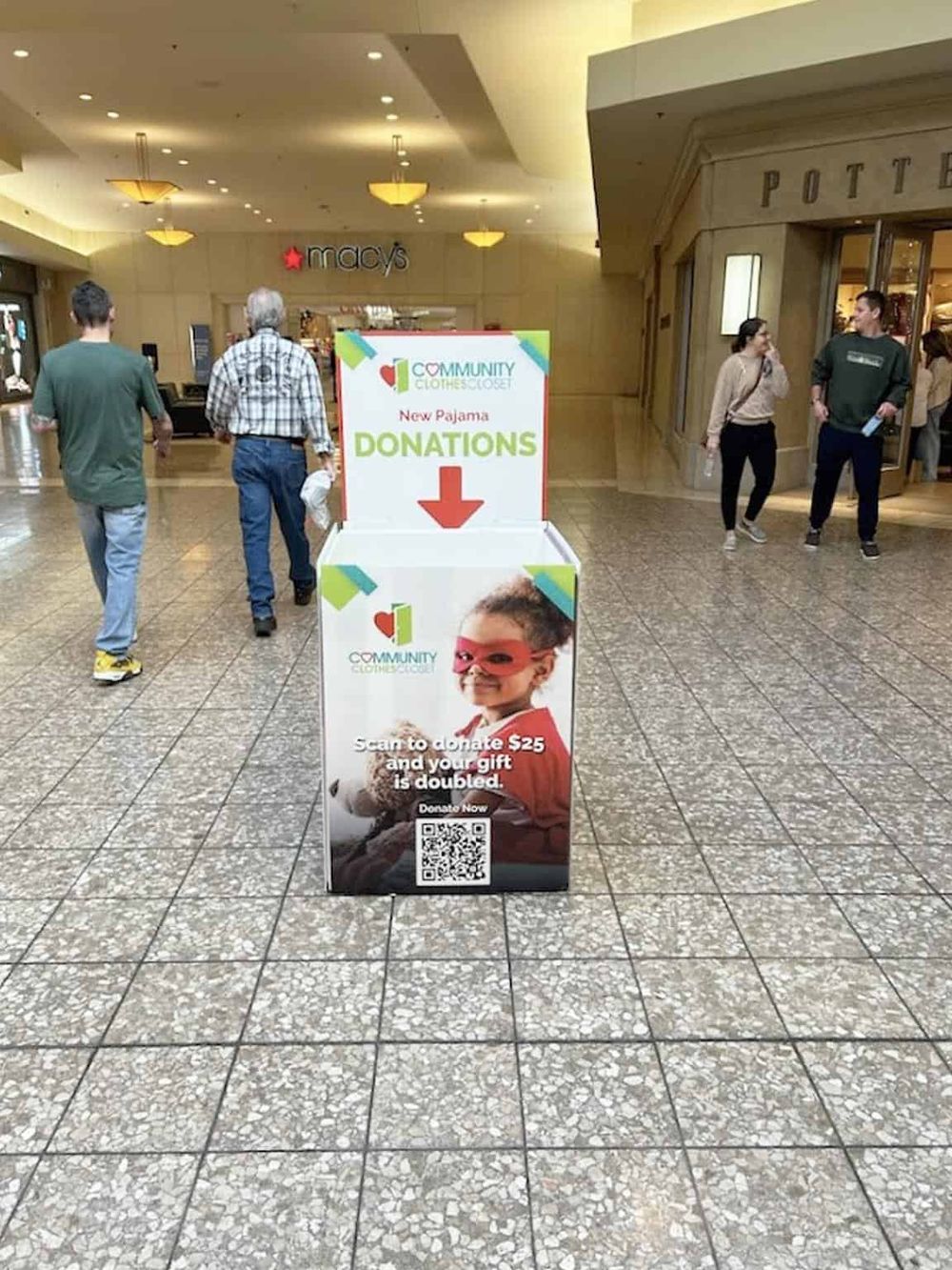Bright donation stand in mall for community clothing charity promoting new pajamas and donations with QR code for contributions.