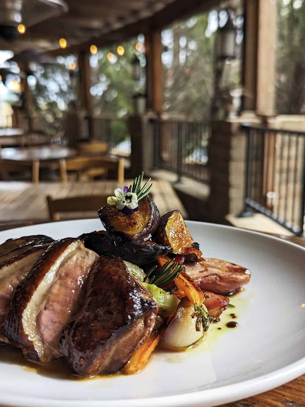 Succulent grilled steak with roasted vegetables and herbs, served on a white plate in rustic restaurant setting.