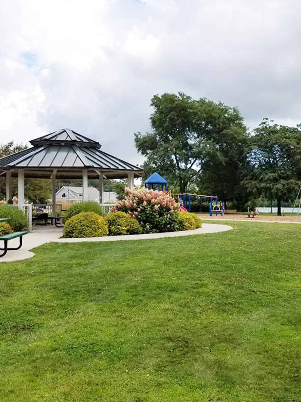 Colorful park with gazebo, children's playground, lush green grass, and trees for outdoor recreation.