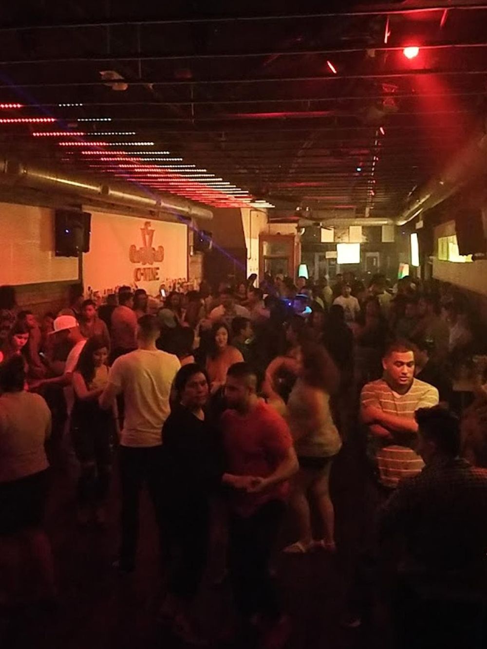 Nightclub scene with people dancing and socializing, vibrant lighting, and lively atmosphere.