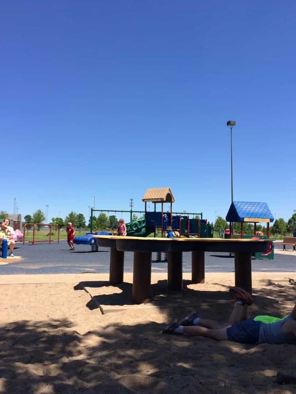 Bright playground with slides, swings, and children playing under clear blue sky at QuestForDirections park.