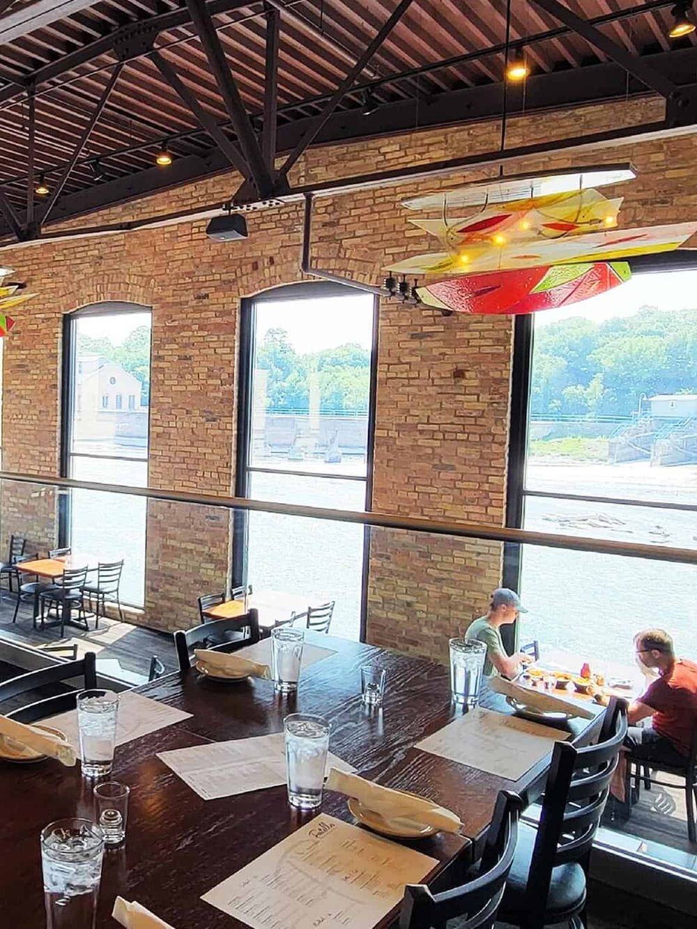 Bright indoor restaurant with large windows, brick walls, and surfboard decor, ideal for dining and gatherings.