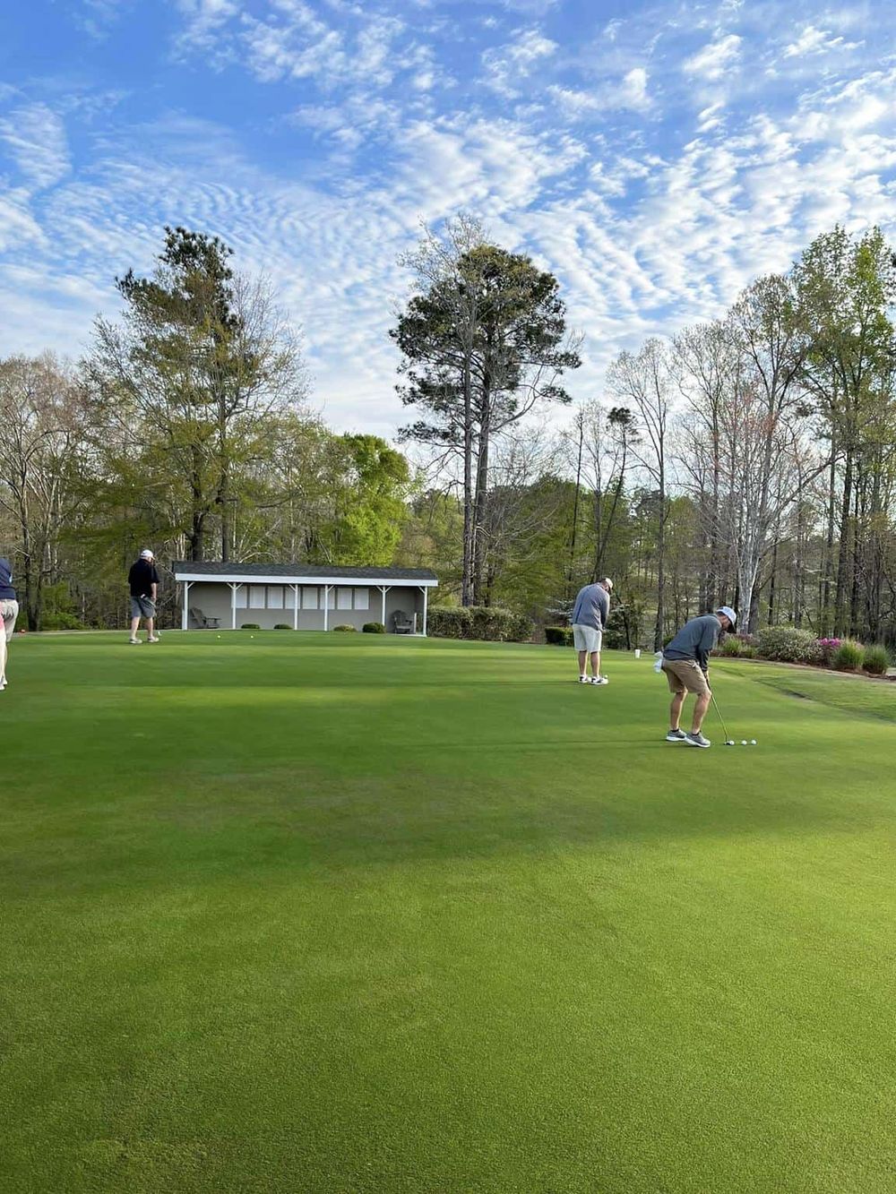 Golfers playing on a lush green golf course under a partly cloudy sky.