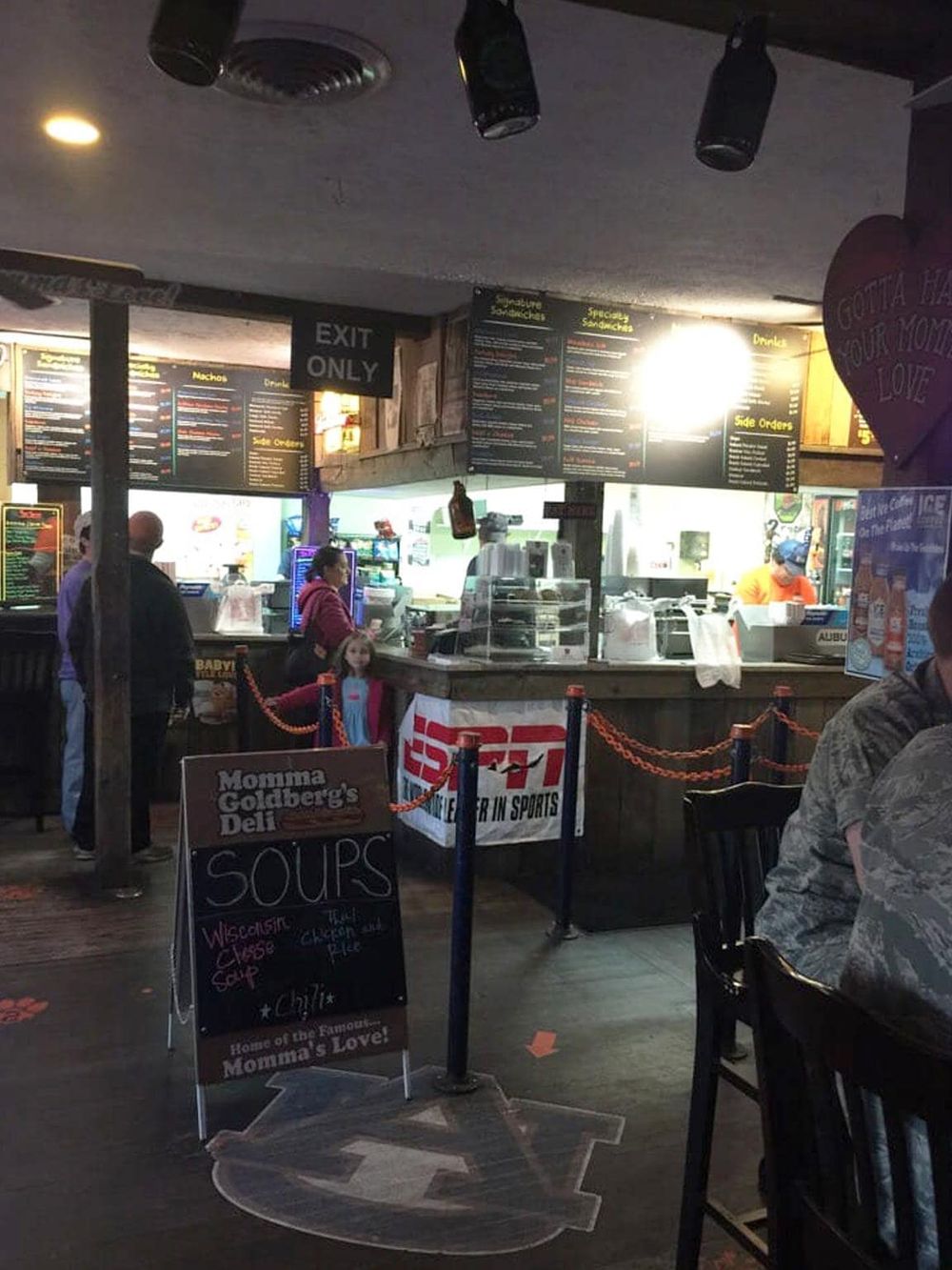Brightly lit fast-food restaurant interior with menu boards, customers, and a chalkboard sign for soups.