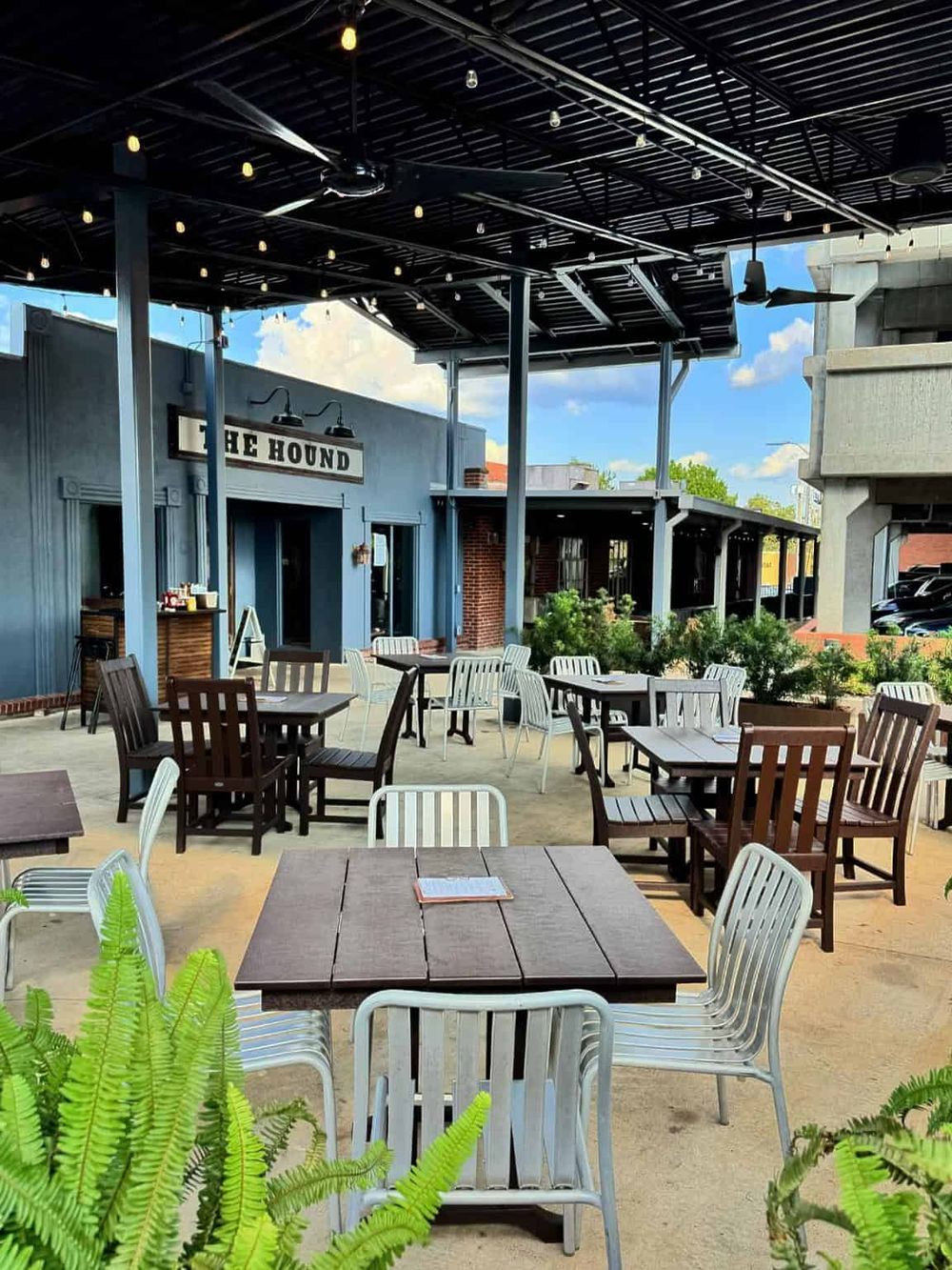 Stylish outdoor patio at The Hound restaurant featuring modern seating with string lights and greenery.