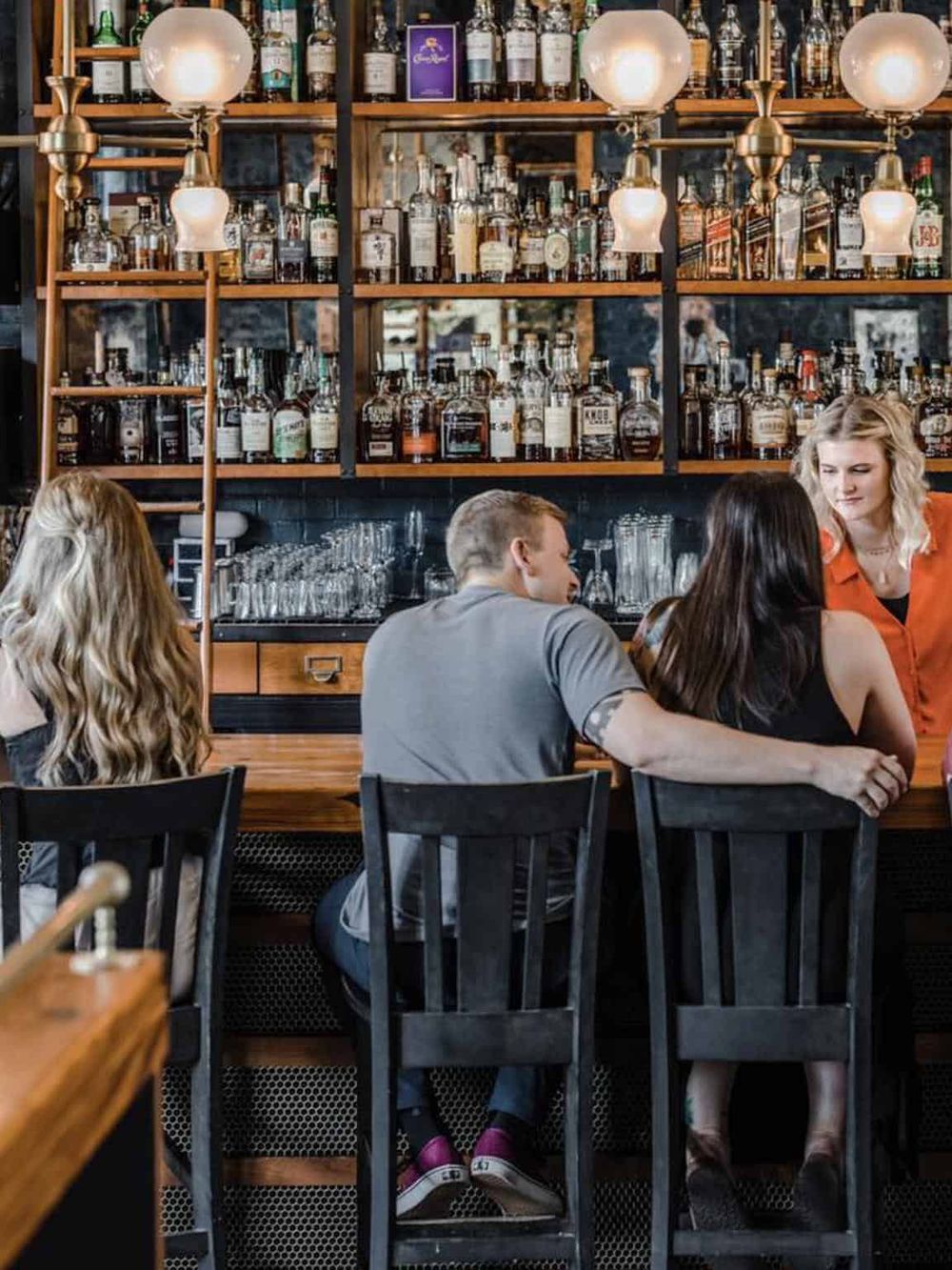 A lively bar scene with patrons socializing at the counter in a trendy, well-stocked bar environment.