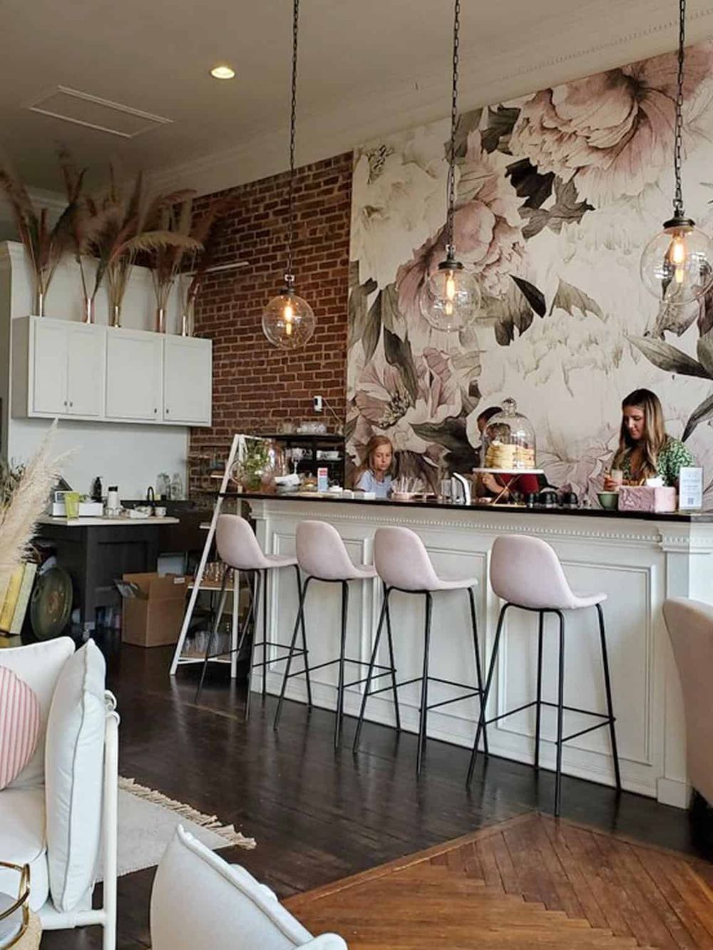 Chic coffee shop interior with floral accent wall, cozy bar seating, and modern pendant lighting. Perfect for a relaxing brunch or coffee break.