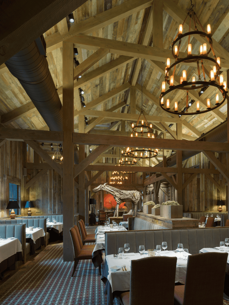 Rustic barn-style restaurant interior with wooden beams, elegant chandeliers, and cozy dining tables.