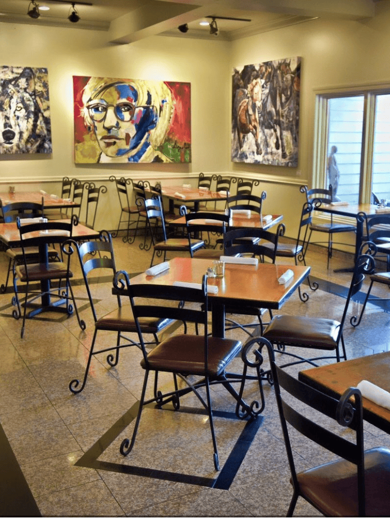 Colorful art gallery interior featuring modern paintings and stylish dining tables and chairs.