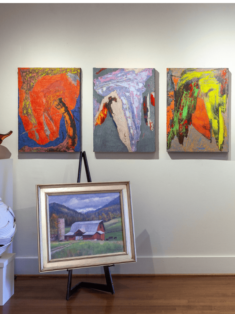Vibrant abstract paintings and a landscape artwork displayed in an art gallery or studio setting.