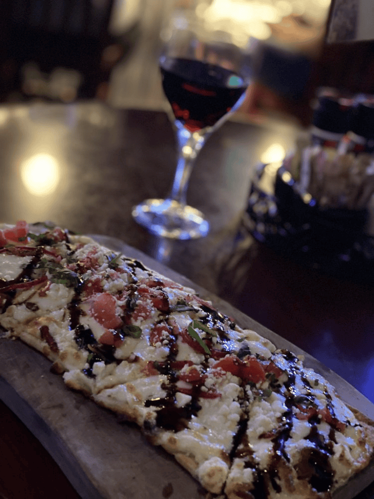 Delicious rectangular pizza with fresh toppings and balsamic glaze, paired with a glass of red wine. Perfect for a cozy dining experience.