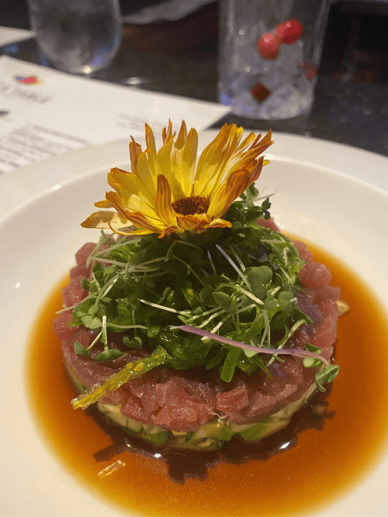 Fresh tuna tartare with microgreens and edible flower on a white plate, showcasing gourmet cuisine.
