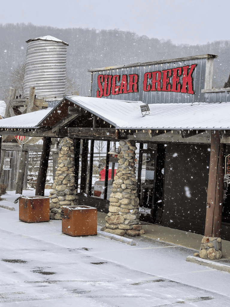 Snow-covered Sugar Creek restaurant exterior with rustic stone pillars and metal signage, winter weather, cozy dining spot.