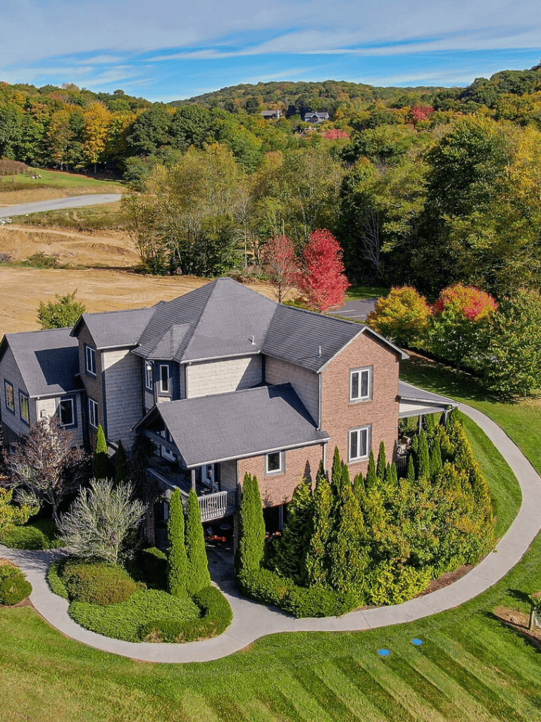 Spacious modern house surrounded by lush trees and landscaped yard, scenic mountain views in the background.