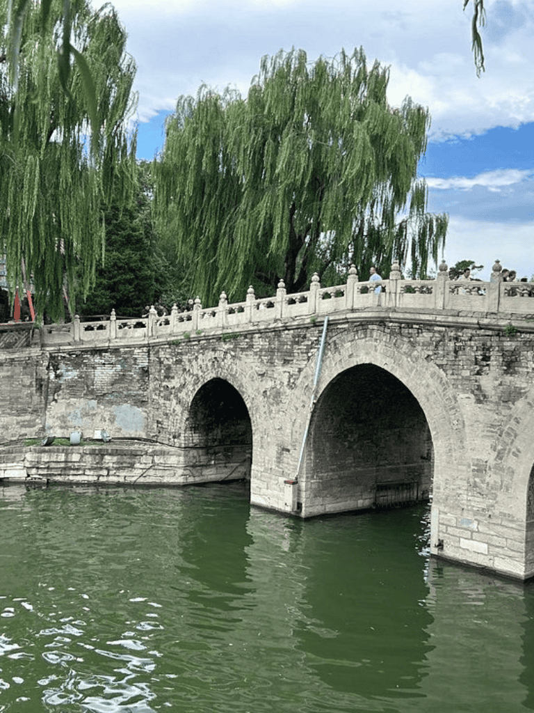 Historic stone bridge over a river with lush green trees in the background.