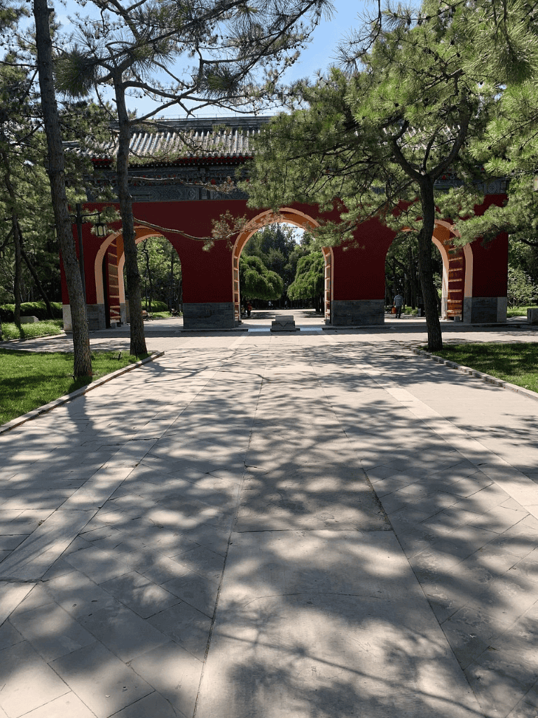 Ancient Chinese archway in a scenic park with trees and sunlight.