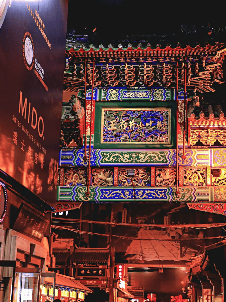 Brightly illuminated traditional Chinese-style building with colorful ornate details and vibrant neon lights at night.