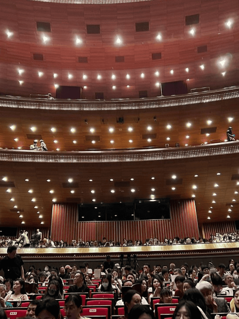 Pledge arena theater with audience and stage, luxurious interior, large event space, modern lighting, high ceiling, wooden accents.