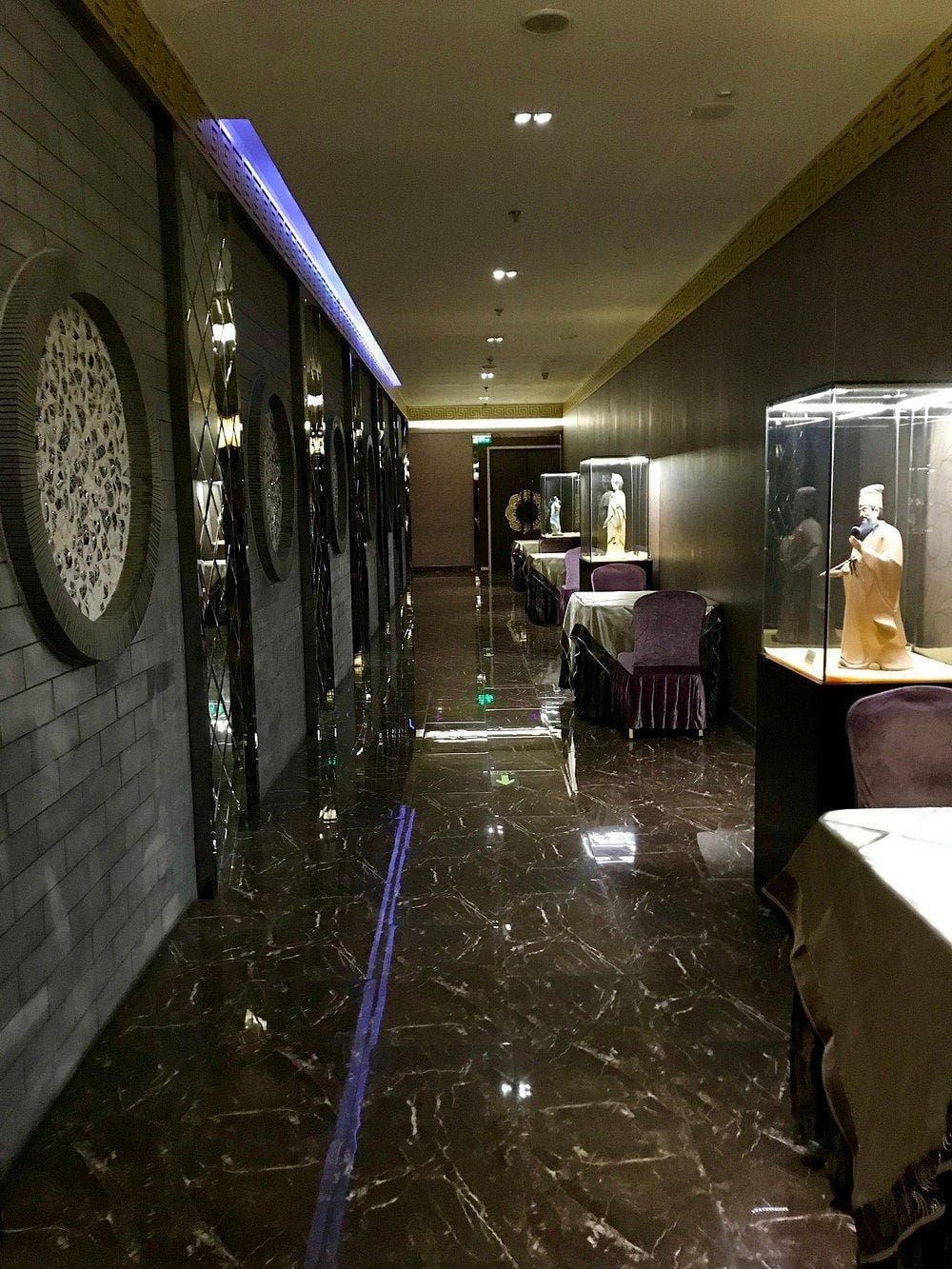 Elegant hallway with display cases of Asian art and statues, polished black marble floor, and sophisticated decor.