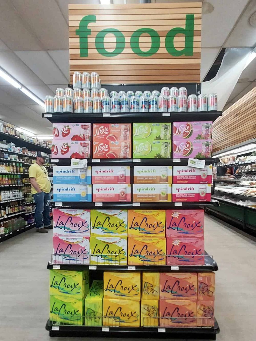 Colorful grocery store display of packaged food and beverages with a "food" sign overhead.