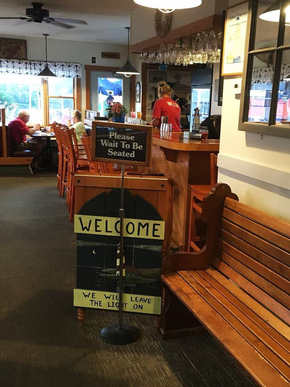 Cozy restaurant interior with welcoming signs, wooden furniture, and customers enjoying meals near windows.