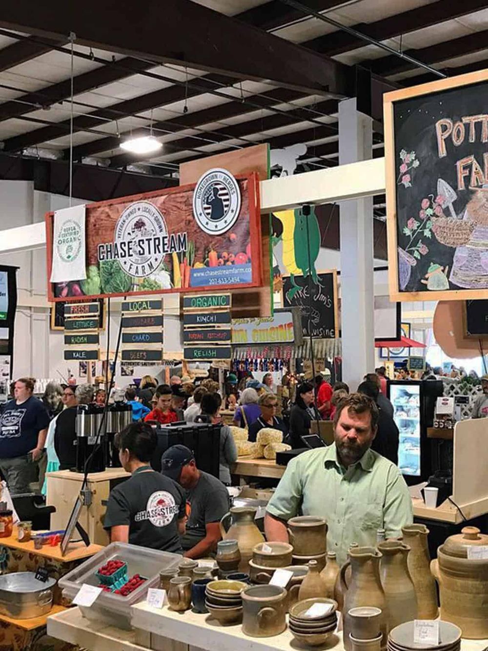 Vibrant indoor farmers market displaying fresh produce, pottery, and diverse local vendors.