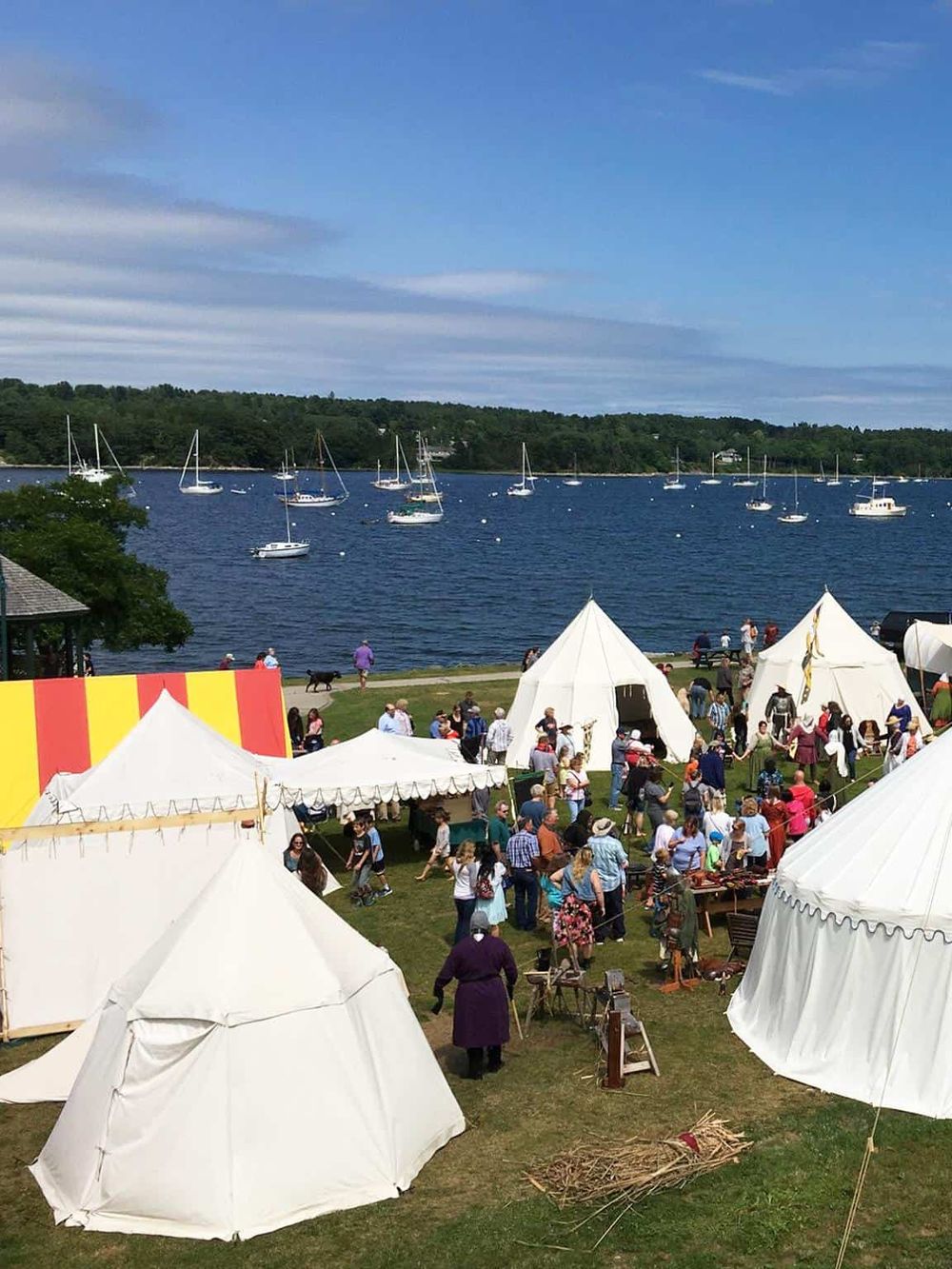 Colorful outdoor event with tents, people, and boats on a lake, ideal for travel and recreational activities.