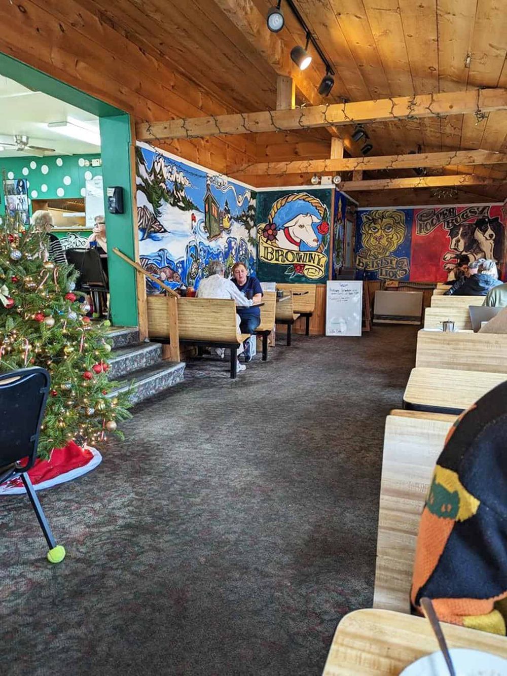 Cozy restaurant interior with colorful murals, wooden ceiling, and holiday decorations, offering a warm dining experience.