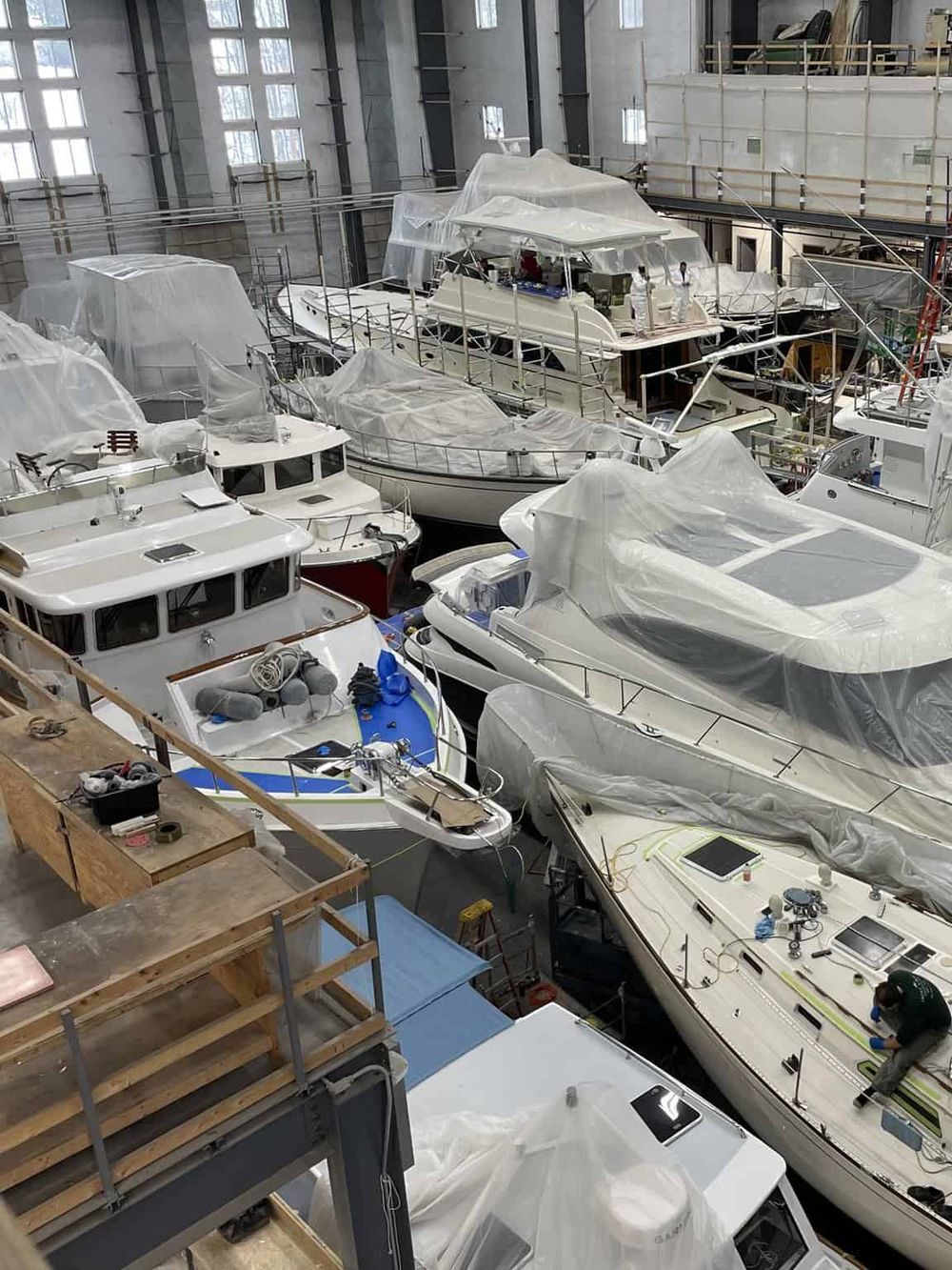 Luxury yacht manufacturing in an indoor shipyard facility with multiple boats under construction.