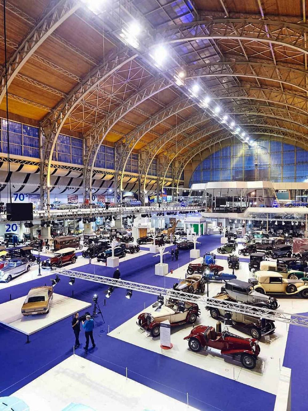 Vintage car exhibition inside a large, well-lit indoor venue with classic automobiles displayed on platforms.