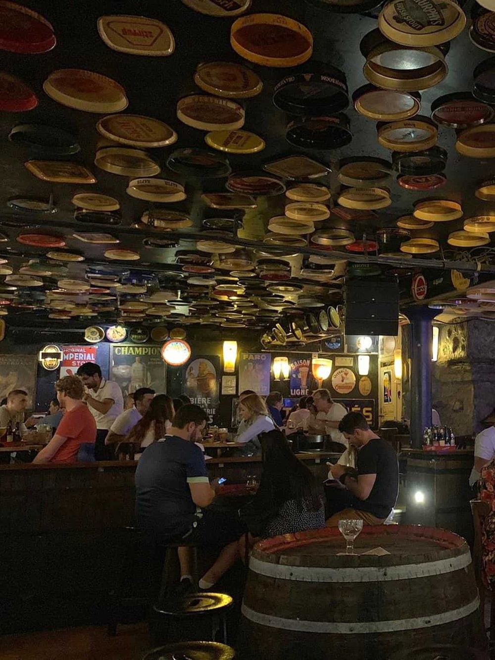 Colorful beer caps ceiling decor at a lively pub or bar with patrons enjoying their drinks.