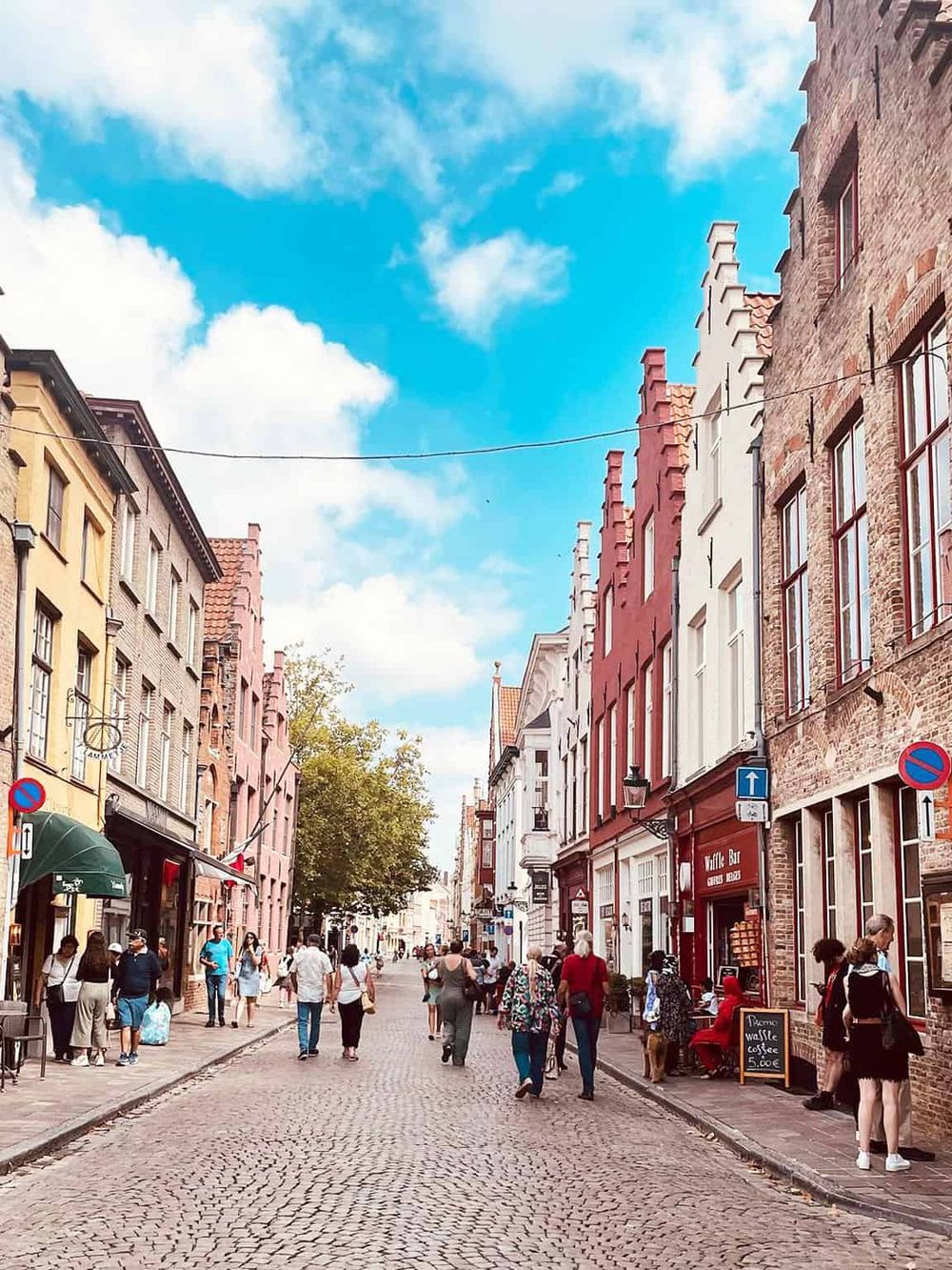 Colorful European street scene, cobblestone road, shops, cafes, people, historic architecture, travel, tourism.