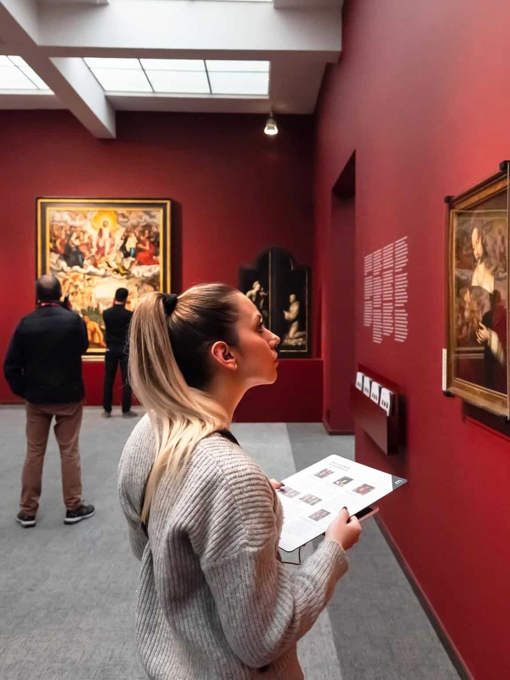 Impression of people enjoying art tour in museum, woman reading exhibit description, vibrant gallery space with classic paintings.