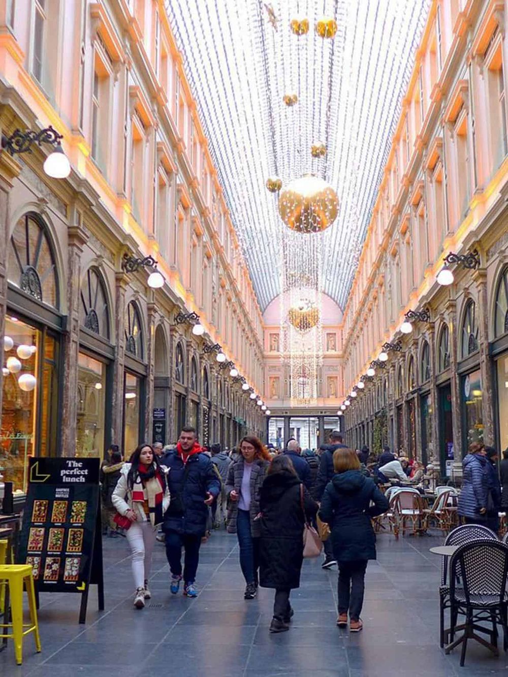 Bright indoor shopping arcade with festive hanging lights and bustling visitors, ideal for retail and dining experiences.