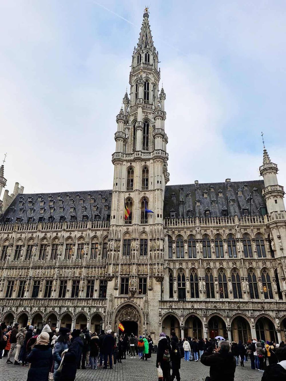 Gothic-style landmark building in Brussels with a tall spire and crowd in front, popular tourist destination.