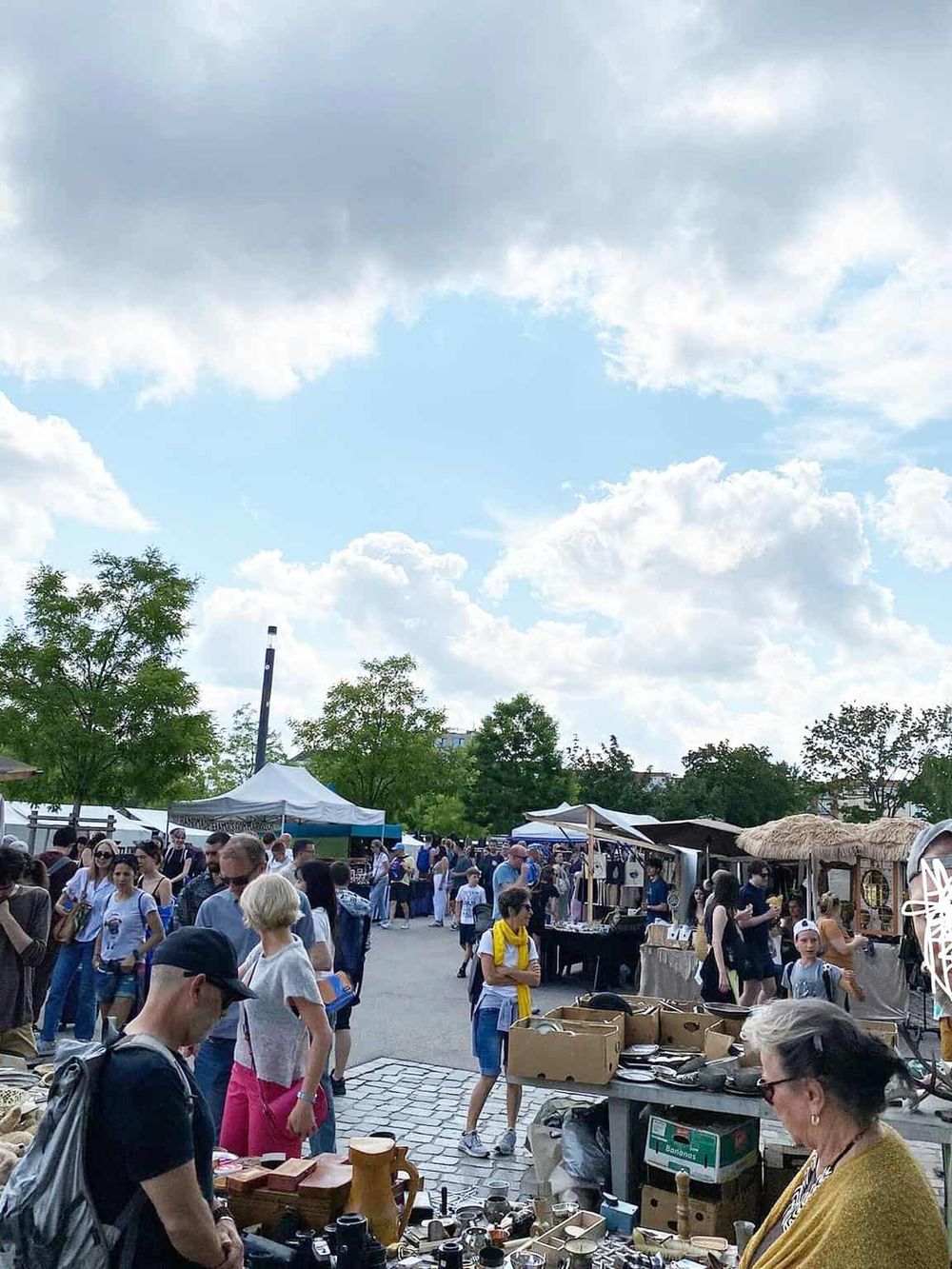 Colorful outdoor market scene with vendors and shoppers under a bright sky.