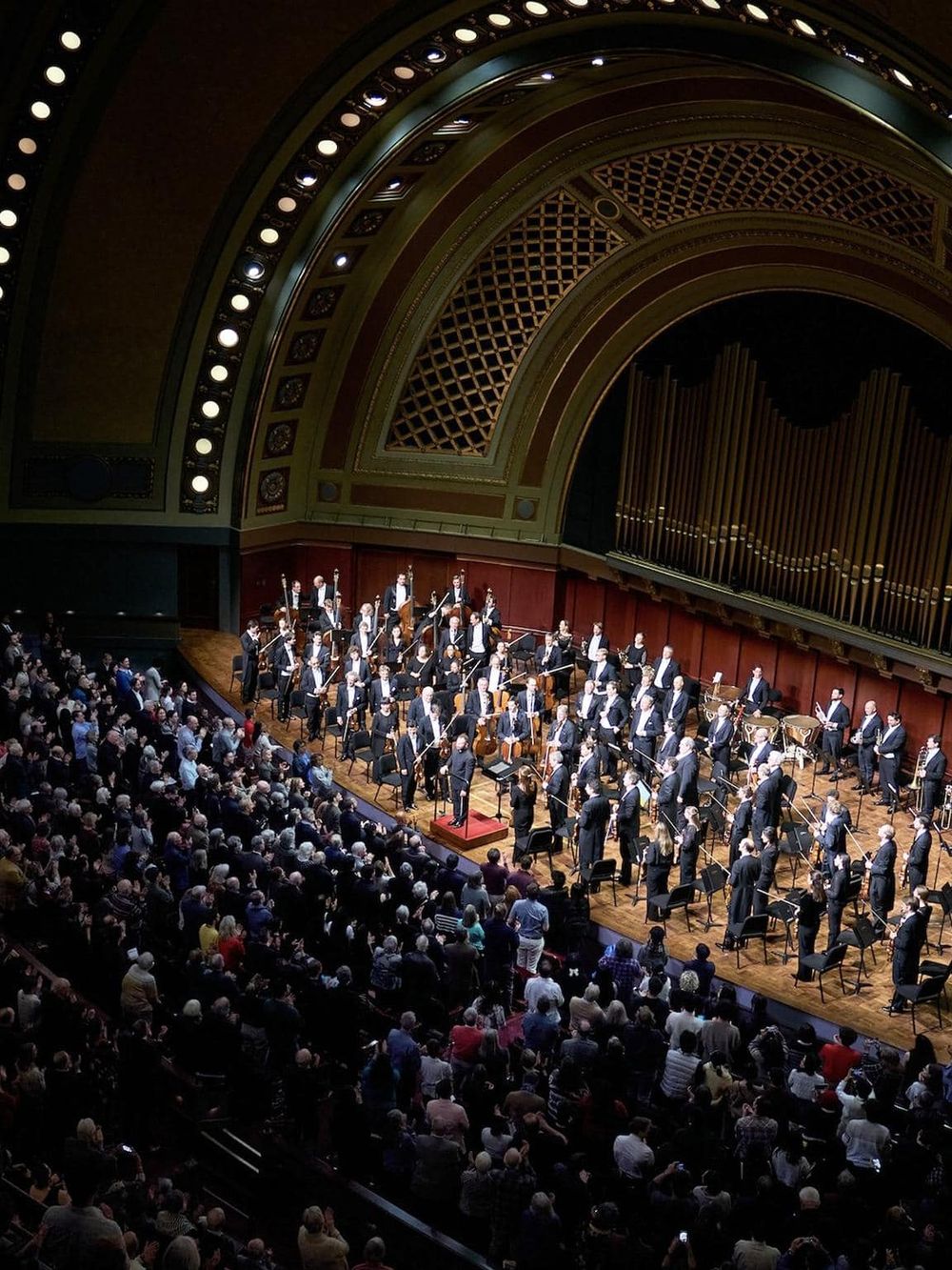 Orchestra performing on stage at a concert hall with an audience in attendance.