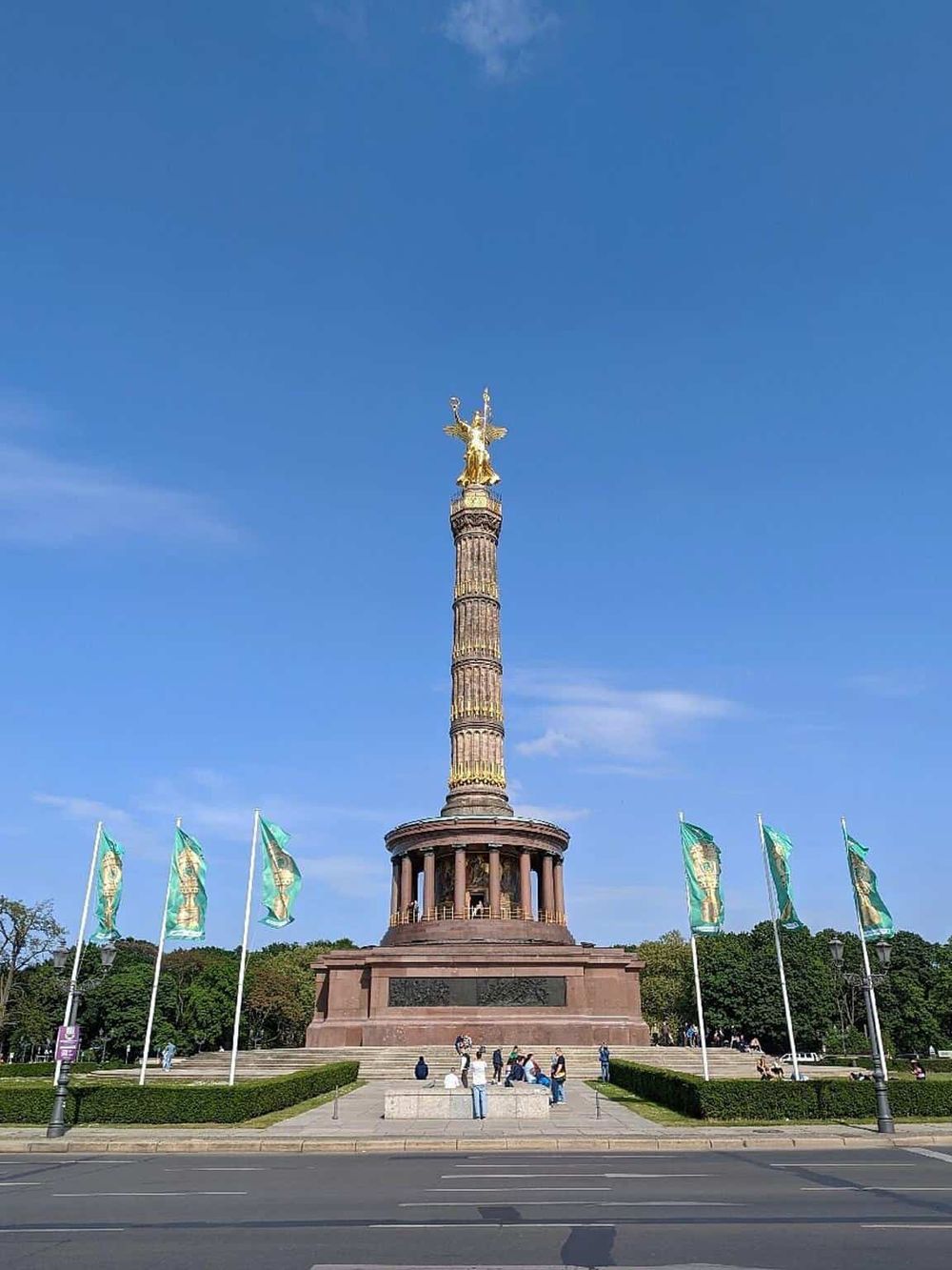 Golden Victory Column monument in Berlin, Germany, under a clear blue sky, with visitors gathering around.