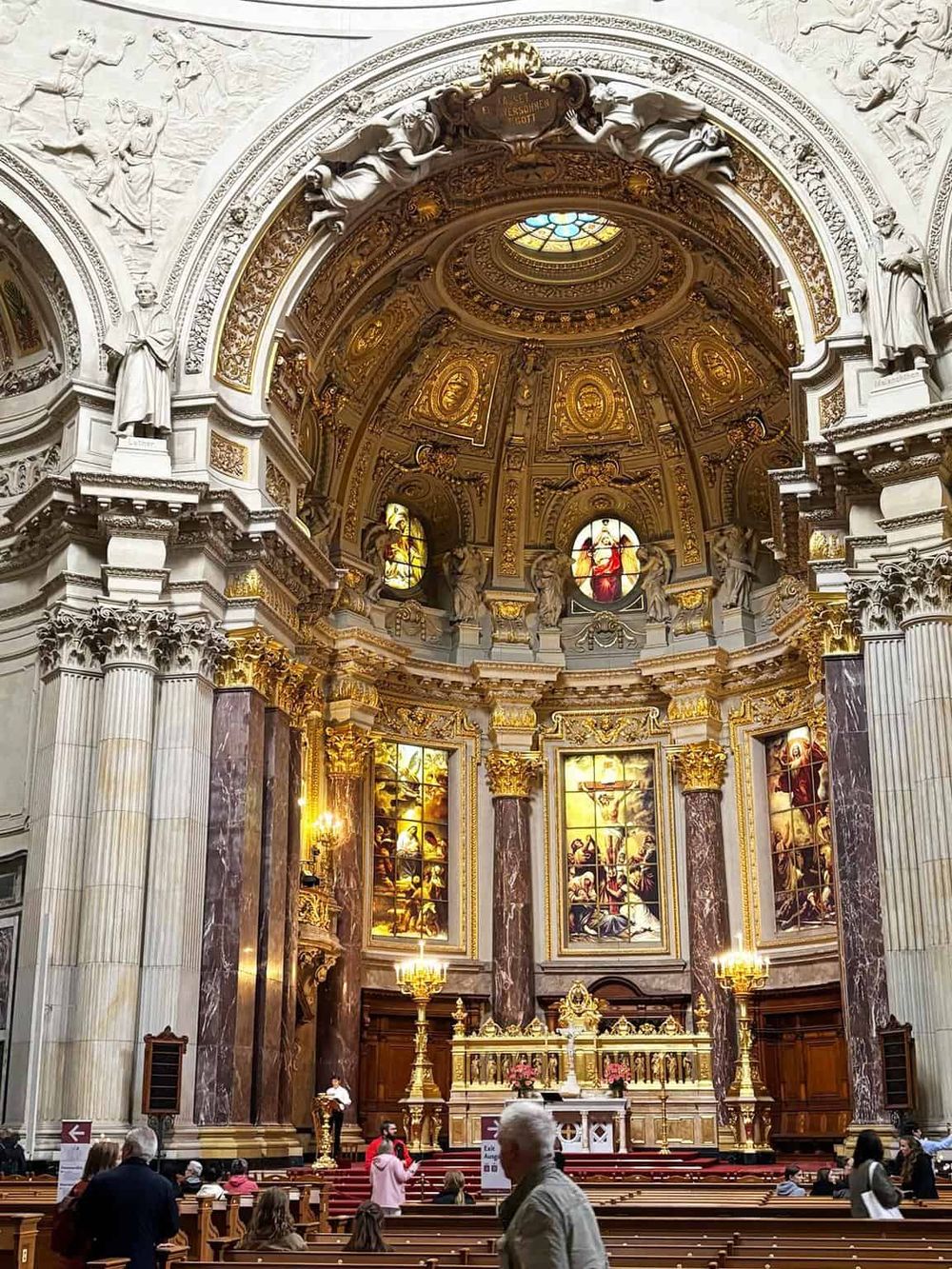 Elegant baroque church interior with ornate gold details, stained glass windows, and an intricate altar design.