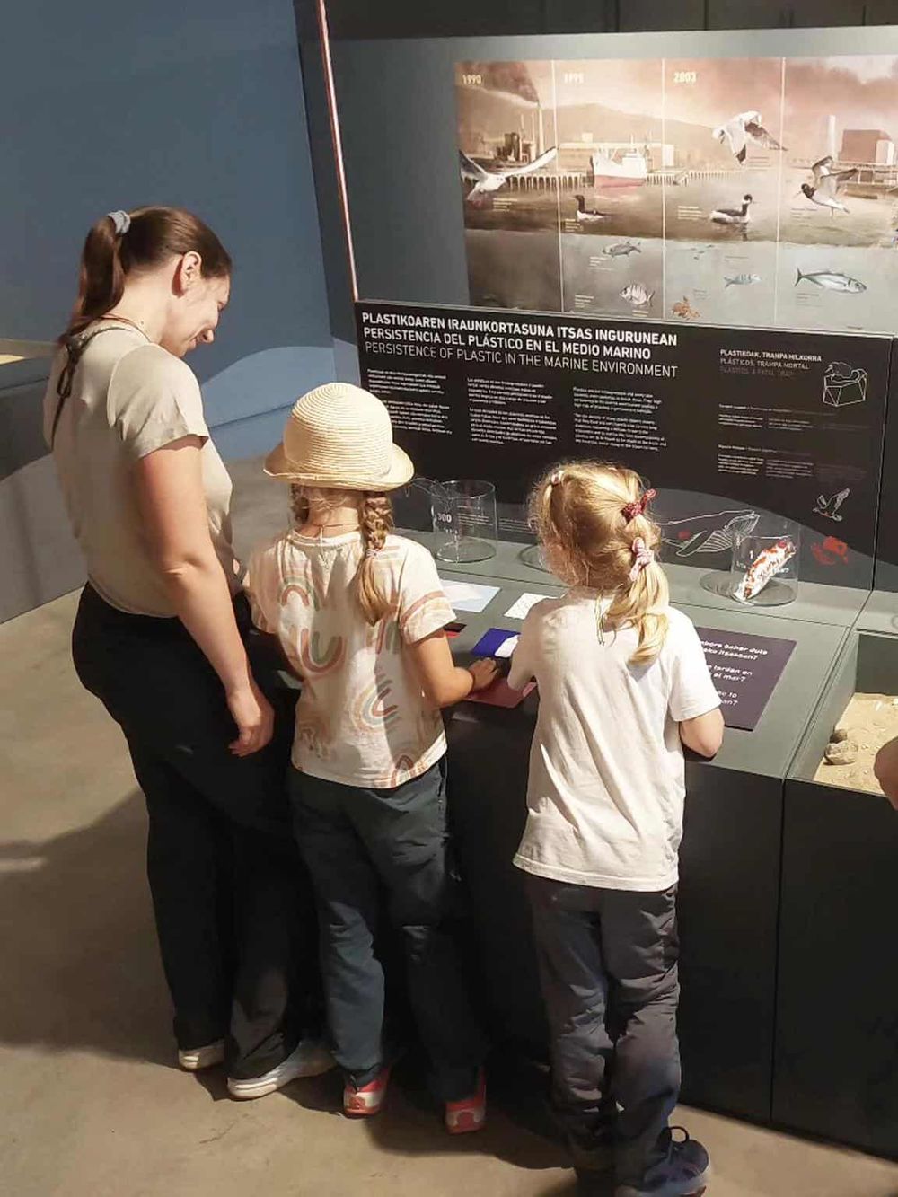 Children exploring marine plastic pollution exhibit at a museum, environmental awareness education, kids learning about plastic waste and marine life.
