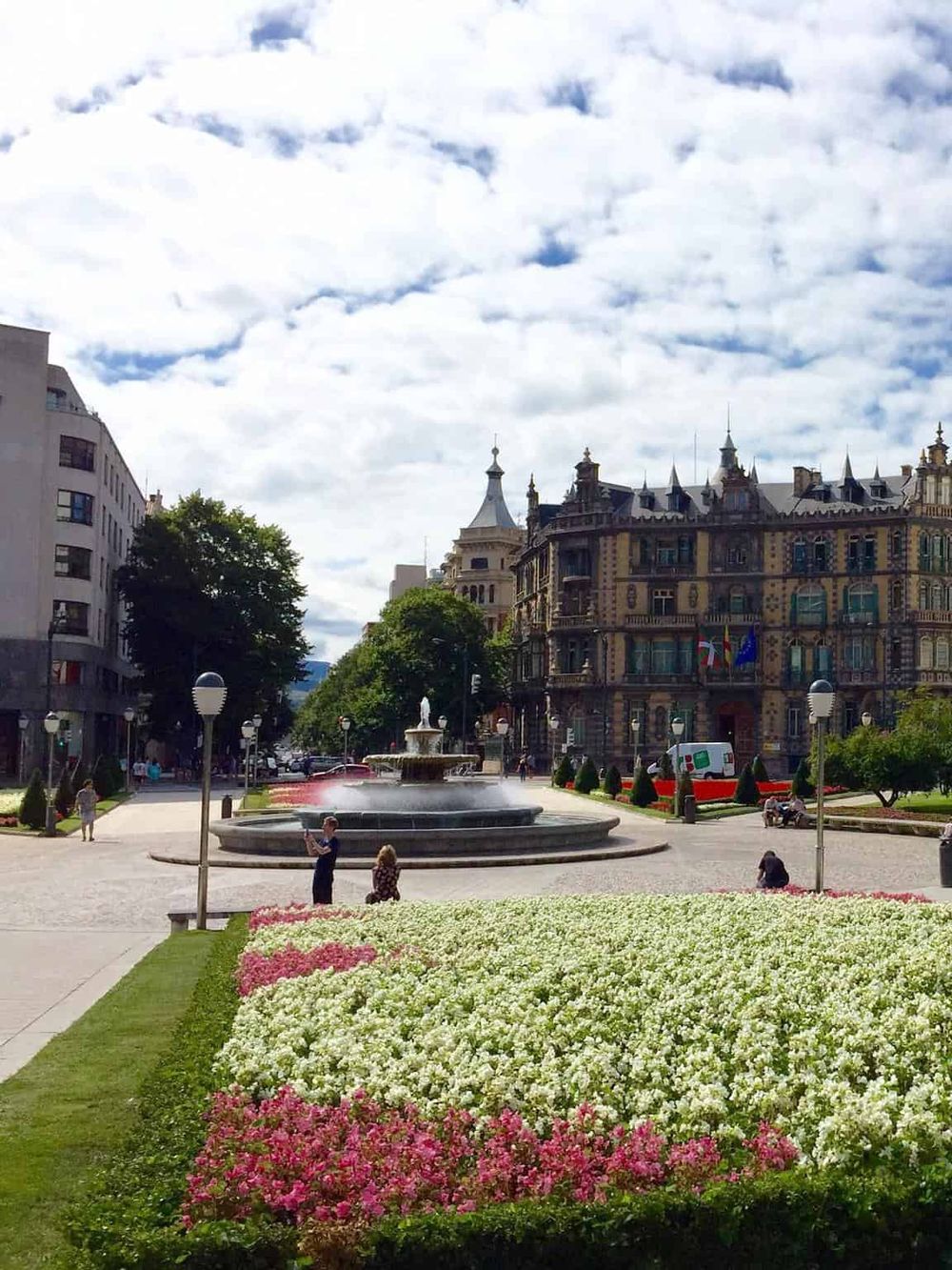 Colorful city square with fountain, historic buildings, and vibrant flower beds in a scenic urban park.
