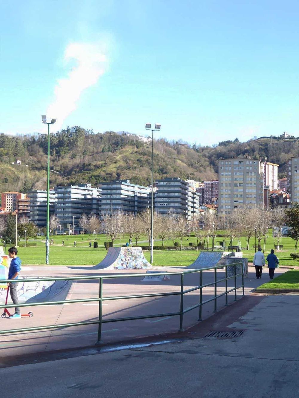 Colorful skate park with cityscape and green hills in the background in a public park.