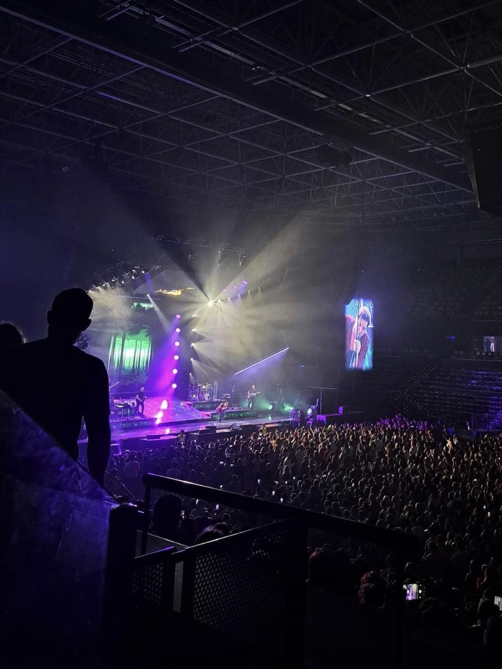 Vibrant concert stage with colorful lights and large digital screens, live music performance in a packed indoor arena.