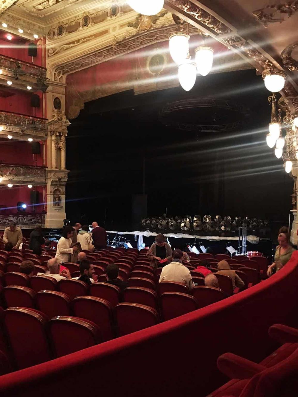Elegant theater interior with ornate gold detailing and plush red seating, preparing for a musical performance.