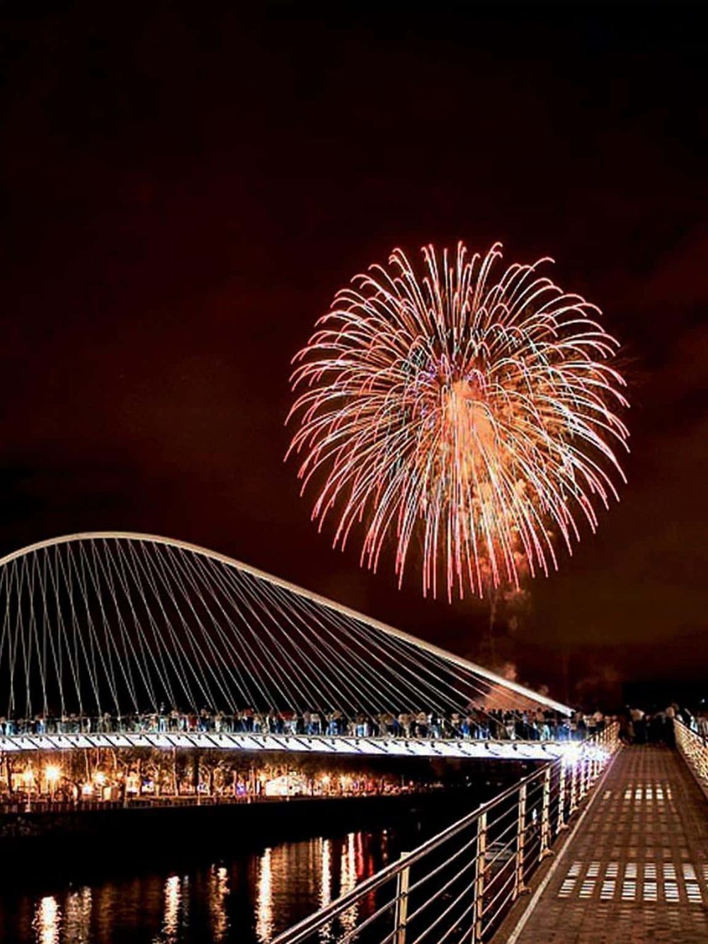 Colorful fireworks display over a modern bridge during night celebration.