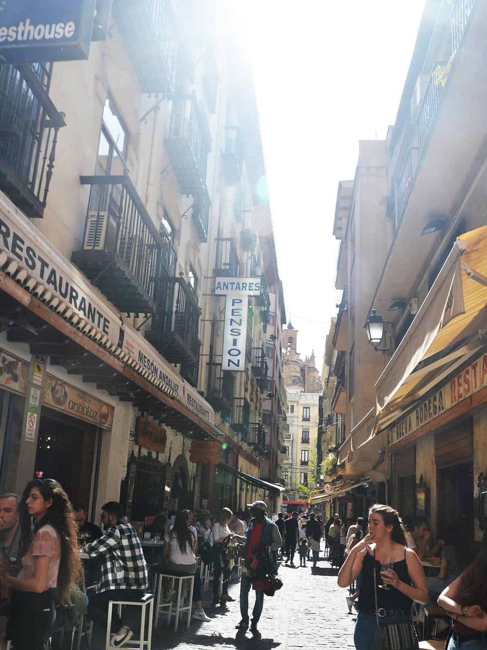 Bustling street with outdoor cafes, pedestrians, and vibrant signs in Madrid, Spain.